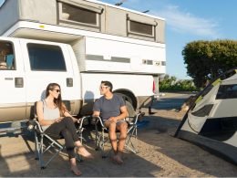 A couple sitting outside a pop up truck camper.