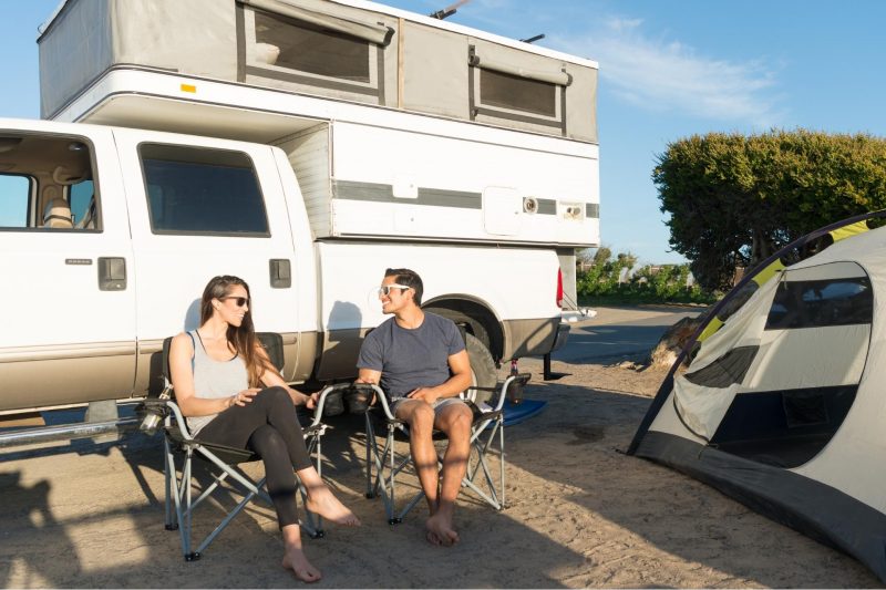 A couple sitting outside a pop up truck camper.