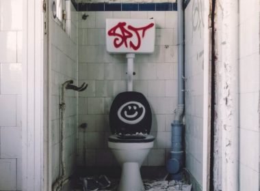 A vandalized public bathroom stall with a black toilet seat and lid with smiley face drawn on it.