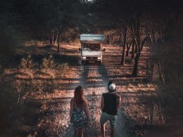 A couple stares down a dirt road at their RV.