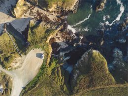 An aeiral view of an RV parked on a cliff near water with waves crashing onto the rocky shore.