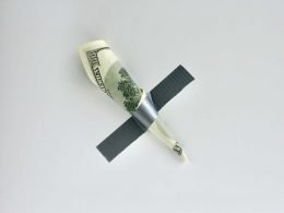 A one hundred dollar bill duct taped to a gray wall.