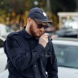 A police office talks into his radio on his shoulder while standing in a parking lot.