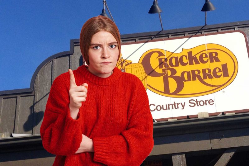An upset woman waves a finger to reprimand in front of the Cracker Barrel building sign.