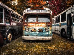 A lineup of rusted and worn vintage buses parked in a field.