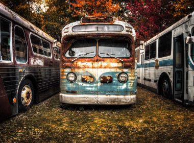 A lineup of rusted and worn vintage buses parked in a field.