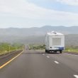 A fifth wheel being towed through the mountains on a smooth, paved road during the day.