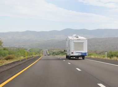 A fifth wheel being towed through the mountains on a smooth, paved road during the day.