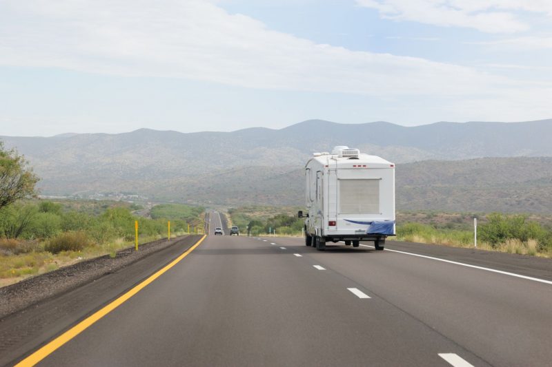 A fifth wheel being towed through the mountains on a smooth, paved road during the day.