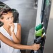 A young women cringes as she reads gas prices at a pump.