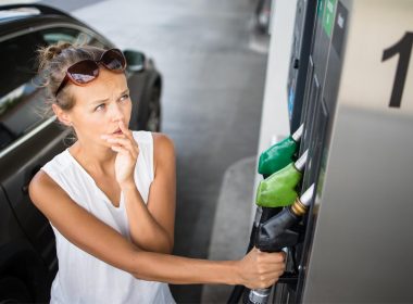 A young women cringes as she reads gas prices at a pump.