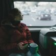 A woman drinking tea in her camper van looks out the window into a parking lot.