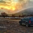 A Nissan Xterra parked on the side of a dirt road as the sun rises over foggy mountains.