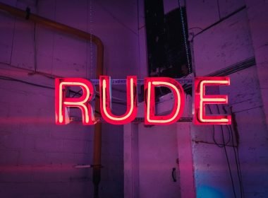An illuminated red neon sign with the word RUDE in capital letters.