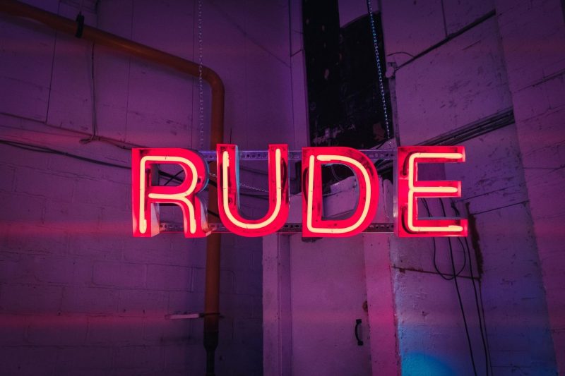An illuminated red neon sign with the word RUDE in capital letters.