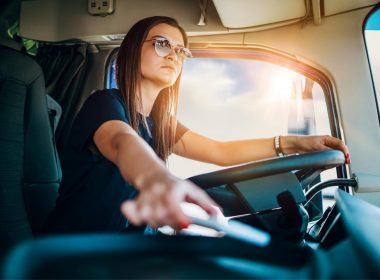 A professional female truck driver with aviator sunglasses driving a semi.