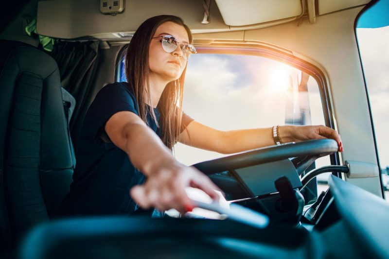 A professional female truck driver with aviator sunglasses driving a semi.