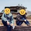 A couple in an argument sitting on a stone wall in front of an RV with sad and angry emojis over their faces.
