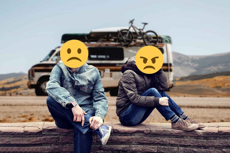 A couple in an argument sitting on a stone wall in front of an RV with sad and angry emojis over their faces.