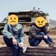 A couple in an argument sitting on a stone wall in front of an RV with sad and angry emojis over their faces.