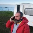 A bearded man makes a concerned phone call in front of his travel trailer.