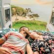 Young couple kissing in the bed of their campervan with a view of the ocean behind them.