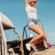A woman jumping up in the air with her hands up in excitement next to her camper van on the beach.