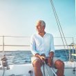 Mature senior man sitting on his sailboat as the wind blows his hair.
