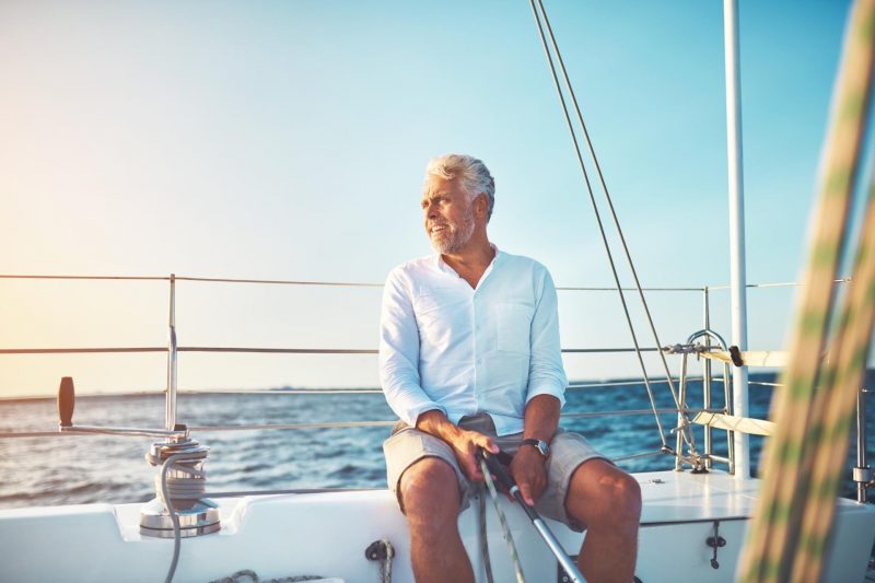 Mature senior man sitting on his sailboat as the wind blows his hair.