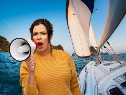 A woman shouting into a megaphone and a sailboat in the background.