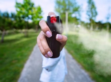 A woman on a path outside holds up and shoots pepper spray from a can towards the camera.