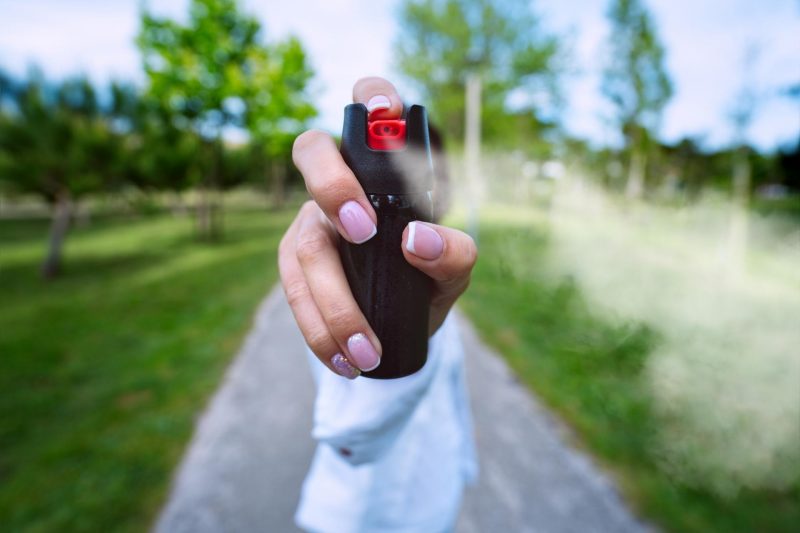 A woman on a path outside holds up and shoots pepper spray from a can towards the camera.