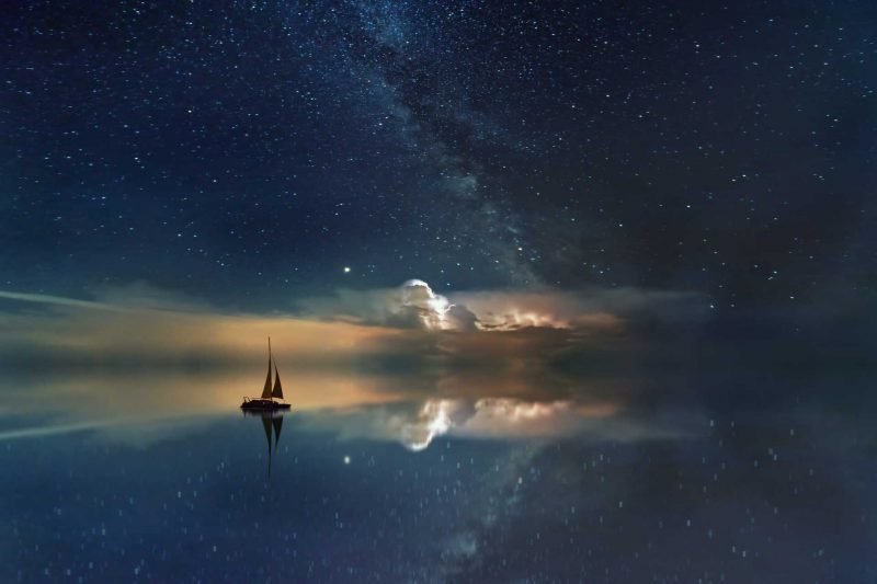 A lone sailboat out in the ocean at night.