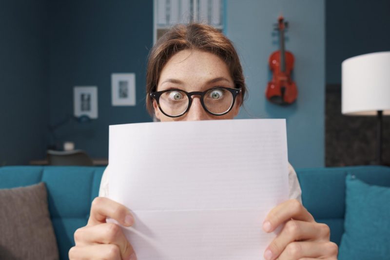 A woman holds up a letter in from of her face and her eyes widen in shock.