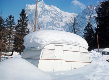 A travel trailer snowed in with a foot of accumulation on the top in the mountains.