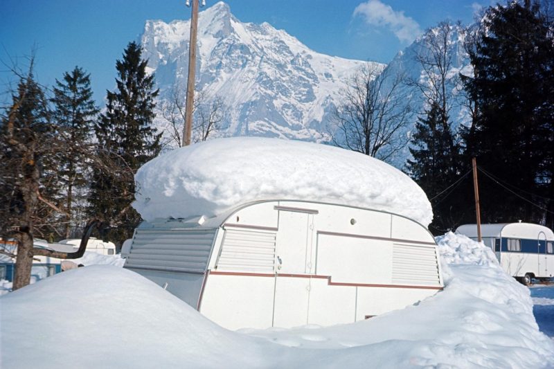 A travel trailer snowed in with a foot of accumulation on the top in the mountains.