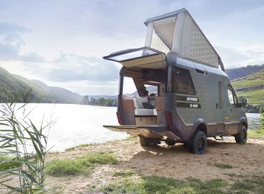Hymer's concept car VisionVenture camper van parked next to a beautiful lake on a summer day, with the popup roof and back patio doors open.