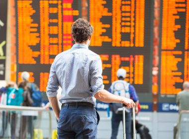 A traveler stands in front of an arrival and departure board in an ariport and sees hundreds of canceled flights.