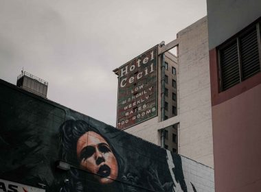 Looking up at the old painted sign for Hotel Cecil in downtown Los Angeles on a cloudy day.