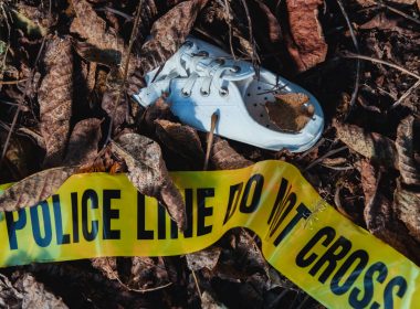 A single white shoe abandoned on the ground near yellow police tape.