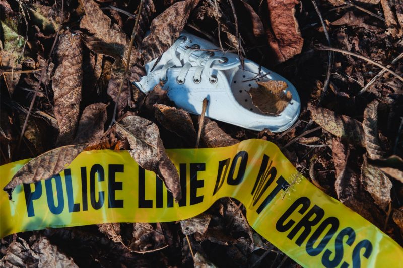 A single white shoe abandoned on the ground near yellow police tape.