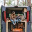 A mother a son enjoy the trees around their campsite from the back of their campervan.