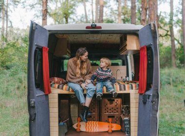 A mother a son enjoy the trees around their campsite from the back of their campervan.