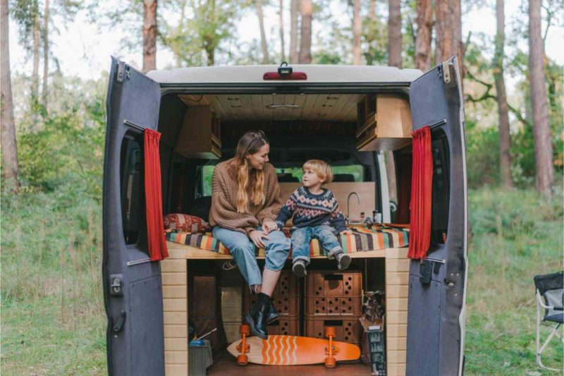 A mother a son enjoy the trees around their campsite from the back of their campervan.