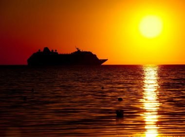 A cruise ship against a golden sunset on the ocean.