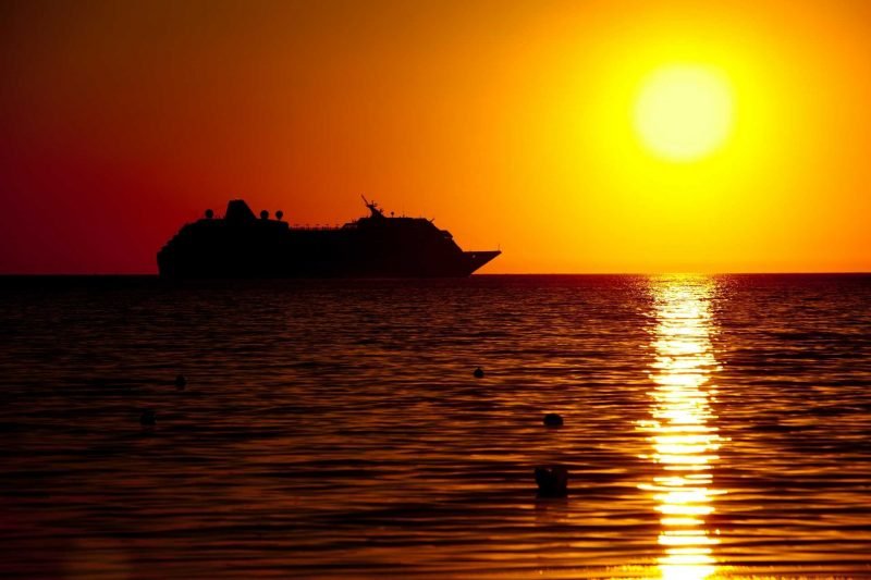 A cruise ship against a golden sunset on the ocean.