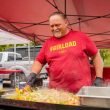 A dad wearing a #girldad shirt grills up food on a flat top in a parking lock during a tailgate party.