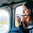 A tourist wearing a headset takes a picture on her phone as she looks out the window of a helicopter.