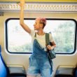 A person holds onto the luggage rack on a train as they smile in anticipation of their travels.