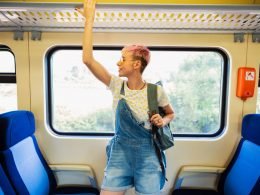 A person holds onto the luggage rack on a train as they smile in anticipation of their travels.
